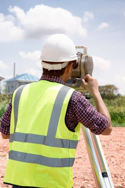 Land surveyor using a total station to locate property line markers on a residential site