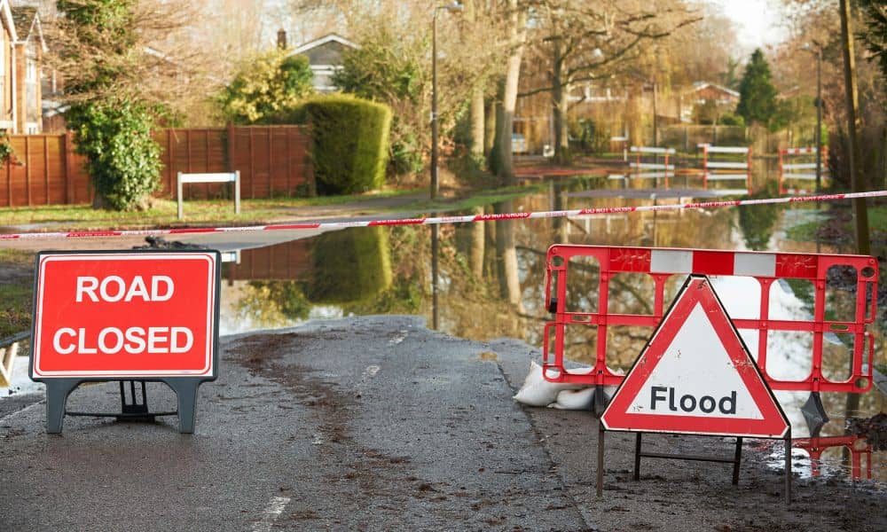 Flooded residential street with warning signs, showing why an elevation certificate is essential before flood season.
