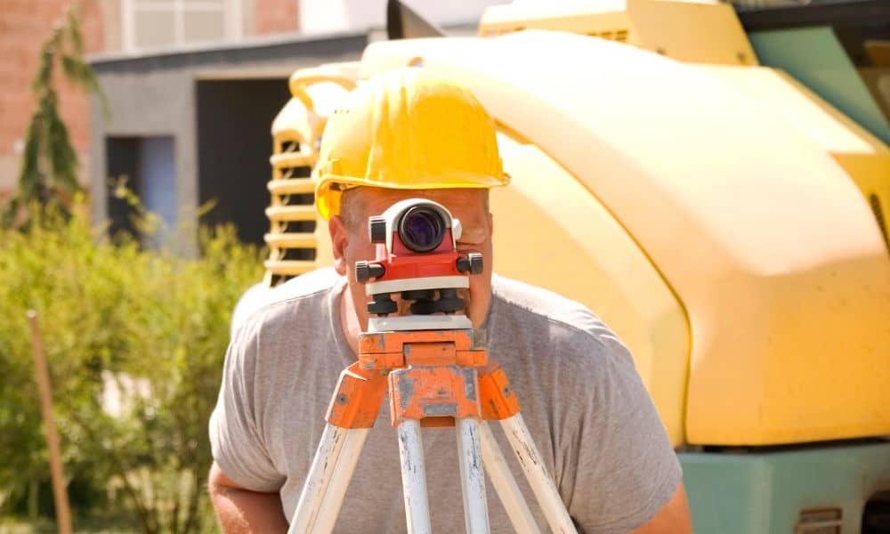 Surveyor using tripod and level to conduct a property survey in front of residential construction under new zoning rules
