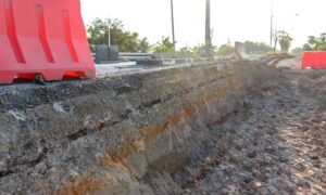 Exposed soil layers along a damaged roadway showing how weak ground conditions can lead to collapses and highlight the need for soil testing