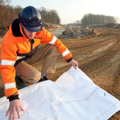 A civil engineer reviewing site plans during a field investigation to determine the cause of pavement failure