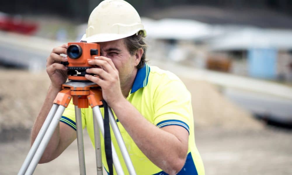 Construction surveyor checking layout with a total station on an active job site during schedule changes