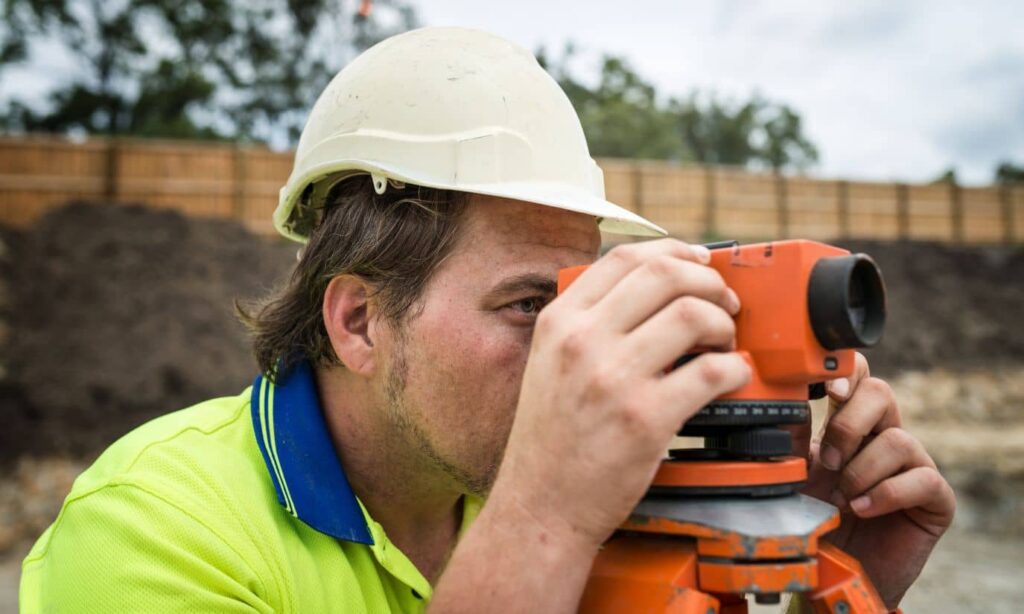 A surveyor using a total station to measure property boundaries on a construction site, illustrating licensed land surveyor work